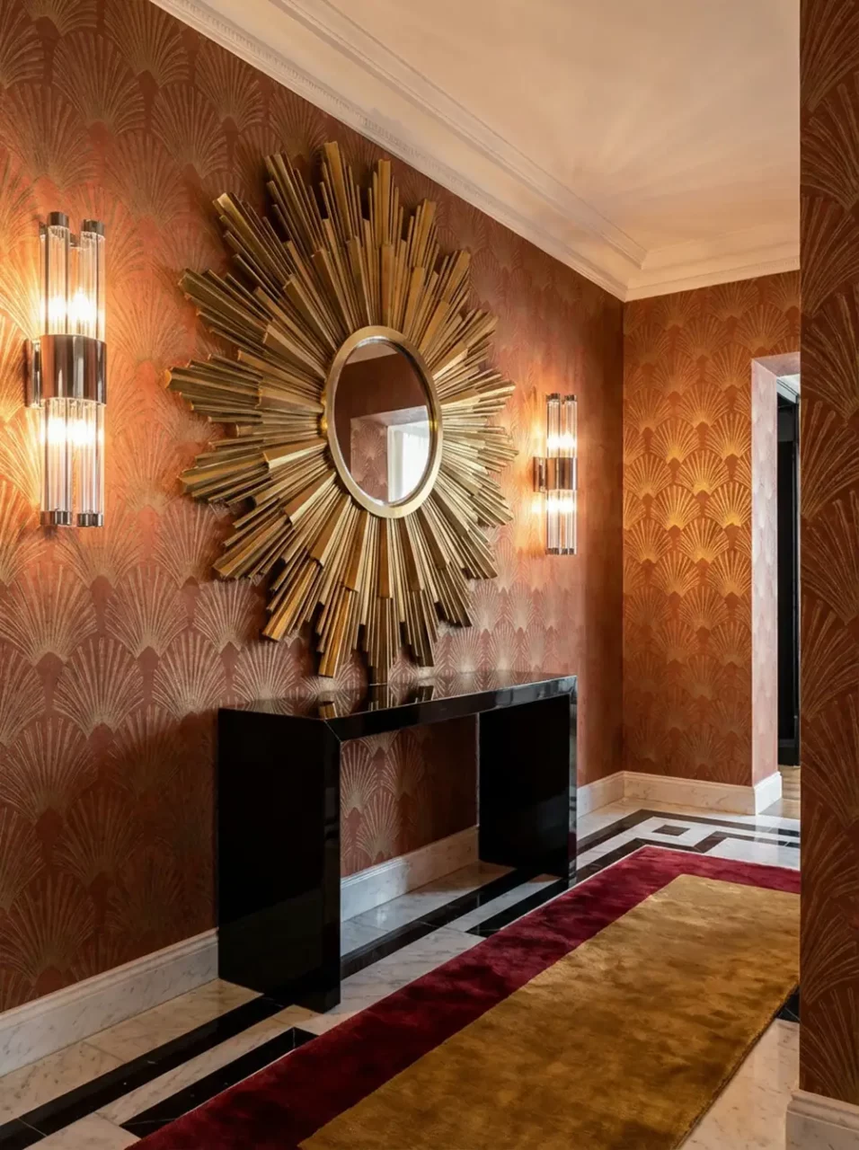 Entrée d'appartement neo art déco avec grand miroir soleil doré, console noire laquée, papier peint éventail terracotta et or